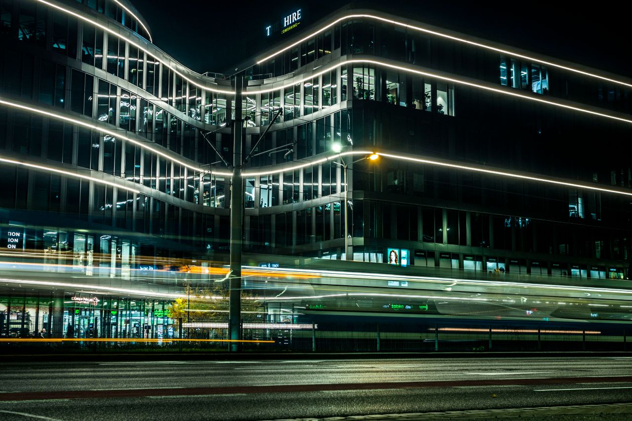 A modern building illuminated at night with dynamic light trails from passing vehicles.